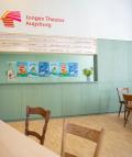Theaterfoyer mit mintgrüner Theke, Holztischen, Stühlen und Logo "Junges Theater Augsburg" an der Wand