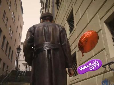 Auf dem Bild zu sehen ist der Schauspieler Erik Völker der als Berthold Brecht in dem für ihn typischen Ledermantel die Stufen des Eisenbergs am Augsburger Rathaus hinaufgeht. In der linken Hand hält ein eine roten Luftballon. Bild von Andreas Horvath