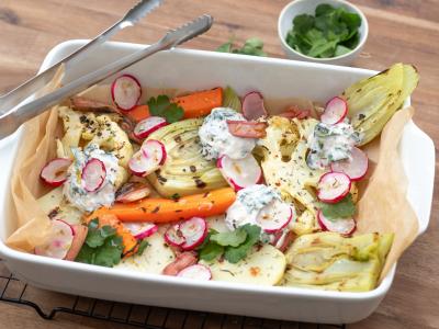 Das Bild zeigt eine bunte Mischung von gegrilltem Gemüse wie Karotten und Radieschen in einer weißen Porzellangrillschale auf einem Bett aus Backpapier. Kleine Inseln von einem Quarkdipp mit Kohlrabi- und Radieschengrün. Das Bild ist von oekokiste e.V.