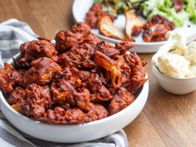 Das Bild zeigt eine kleine Schüssel mit rotbraunen Blumenkohlröschen auf einem grauweiß gestreiften Tischtuch. Daneben befindet sich eine weitere Schüssel mit Blumenkohlröschen Natur auf dem blanken Holz des Tisches. Foto Oekokiste e.V.