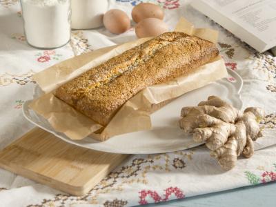 Das Bild zeigt einen Ingerkuchen in der Backform auf einem gestickten Tischtuch. Daneben sind Eier, Mehl und eine Ingwerknolle zu sehen. Bild Oekokiste e.V.