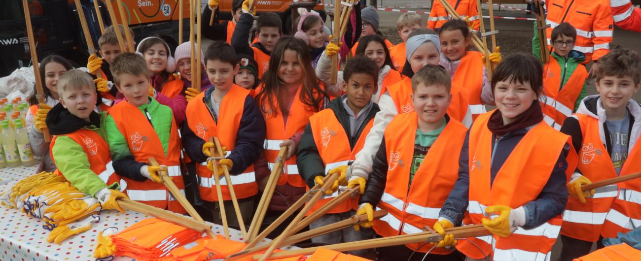 Hier sieht man Kinder als fleißige Helfer*innen von der Müllsammelaktion "Augsburg - Sauber ist in!" im Jahr 2024 in ihrer neon-orangen Warnweste mit passendem Equipment.