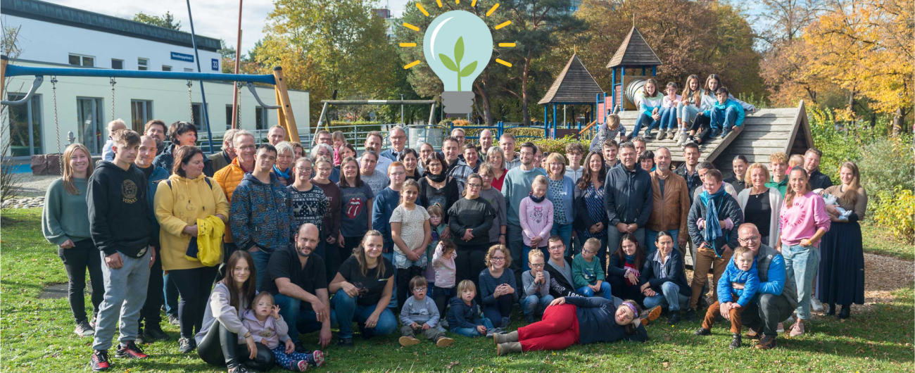 Foto zeigt eine Gruppe des einsmehr Vereins. Ein Gruppenfoto mit vielfältigen Menschen jeglicher Altersklasse. In der ersten Reihe sitzen oder liegen die Personen auf der Wiese, damit alle auf dem Foto sind.