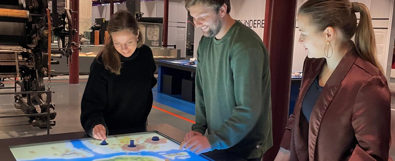 Foto zeigt den neuen digitalen Spieltisch im Textil- und Industriemuseum Augsburg. Drei Personen bedienen gerade das Spiel, um es vorzustellen. Sie haben  das Spiel mitentwickelt.
