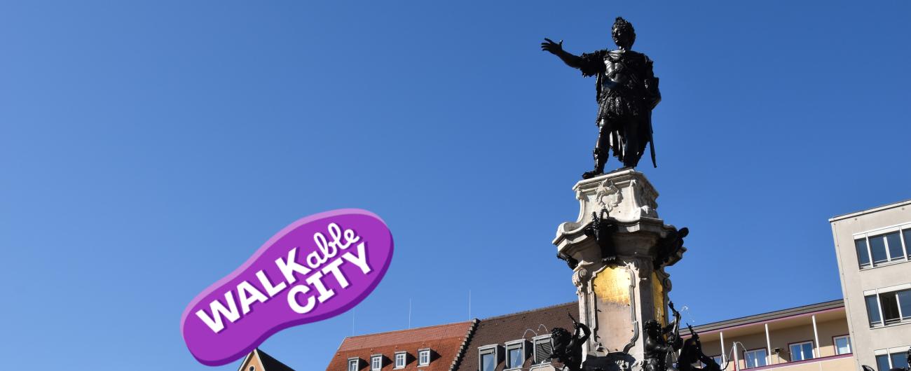 Das Bild zeigt den Augustusbrunnen am Rathausplatz mit der Figur des Kaisers Augustus, der die Hand ausstreckt. Foto Cynthia Matuszewski