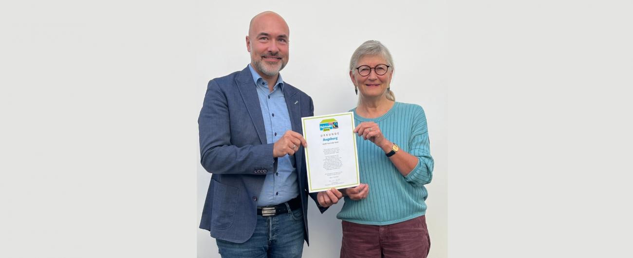 Gesellschafts-Referent Martin Schenkelberg und Ute Michallik von der Steuerungsgruppe Fairtrade-Stadt Augsburg präsentieren die Urkunde zur erneuten Auszeichnung der Stadt Augsburg als Fairtrade-Stadt. Foto: Torsten Mertz