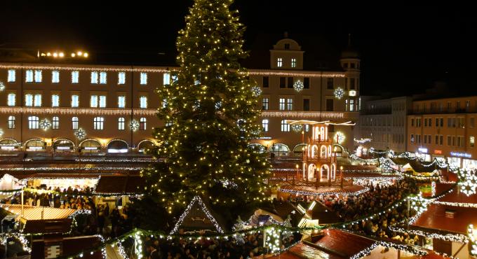Foto zeigt den Augsburger Christkindlesmarkt bei Nacht von oben. Es leuchten überall die Lichterketten in der Mitte ragt der Weihnachtsbaum empor.