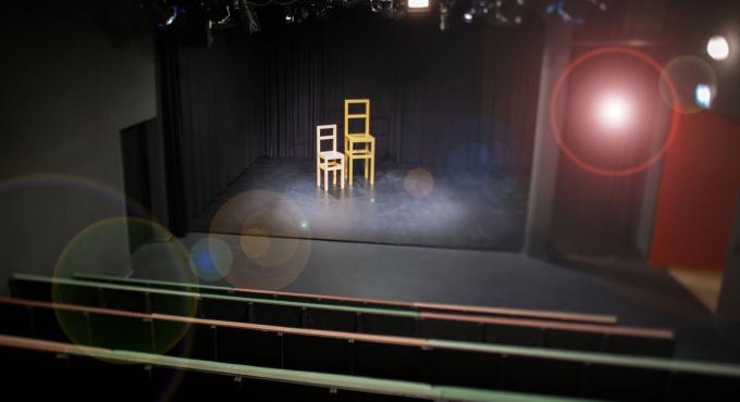 Theaterbühne mit zwei Stühlen in Gelb und Weiß, schwarzem Vorhang und Bühnenscheinwerfern