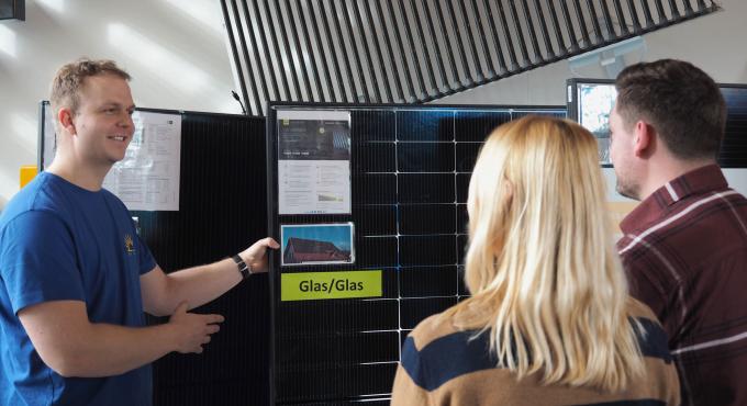 Hörmann Solartechnik Berater erklärt einem Paar ein Glas-Glas-Solarmodul im Ausstellungsraum.