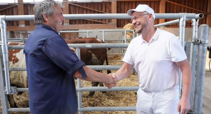 Zwei Menschen, die sich die Hand schütteln in einem Kuhstall: Tagwerk Landwirt Toni Wollschläger und Betriebsleiter Tagwerk Biometzgerei Jürgen Weig