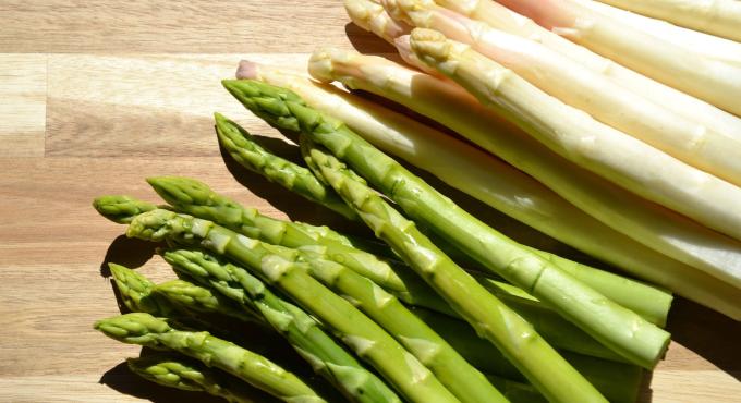 Grüner und weißer Spargel nebeneinander auf einem Holzuntergrund.