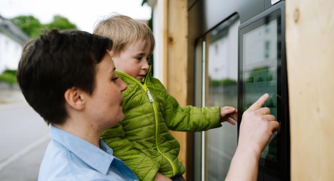Frau mit Kind vor einem Automaten, in dem es Eis zu kaufen gibt.